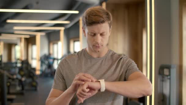 Leende kroppsbyggare med smart klocka på gymmet. Sportsman stående i fitness klubb — Stockvideo