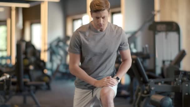 Attraktiv konditionsman värmer upp ben på gymmet. Sportsman gör knäböj på gymmet. — Stockvideo