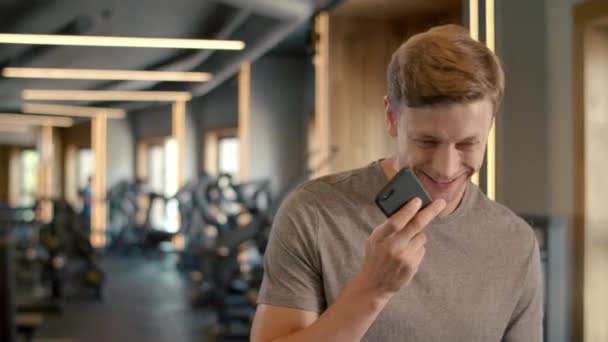 Alegre culturista hablando por teléfono en el gimnasio. Deportista de pie en el club deportivo — Vídeos de Stock