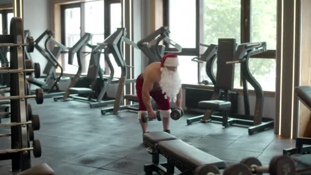 圣诞老人在体育馆里做哑铃摆动.体育俱乐部穿着桑塔服装的男人 — 图库视频影像