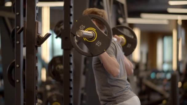 Homem fitness jovem fazendo agachamentos barbell no ginásio. Treinamento de desportista em clube desportivo — Vídeo de Stock