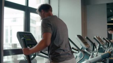 Formda adam spor kulübünde ısınıyor. Spor salonunda eliptik antrenör kullanan erkek sporcu