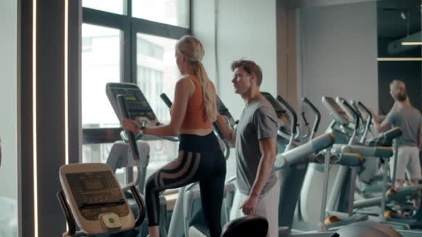 Sexig passform tjej med hjälp av elliptisk tränare i sportklubben. Par träning på gym — Stockvideo