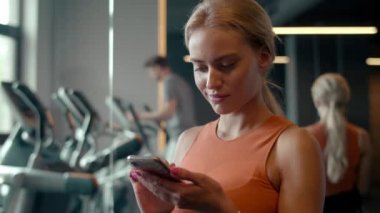 Spor salonunda formda bir kız mesaj atıyor. Spor kulübünde cep telefonu kullanan spor kadını.