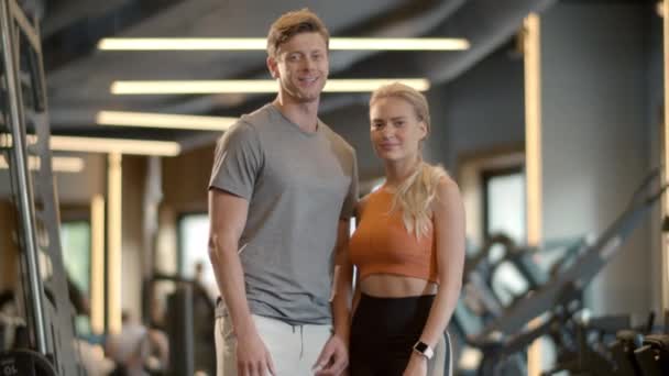 Fröhliches Paar genießt Erfolge im Sportverein. Fitter Mann zeigt wie Zeichen im Fitnessstudio — Stockvideo