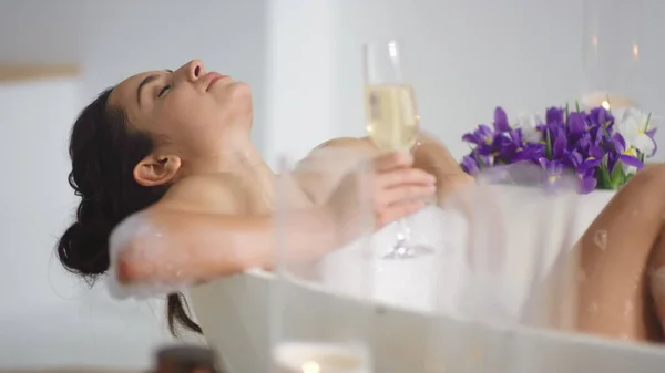 Linda chica descansando en la bañera moderna. Relajada chica acostada en el baño con champán — Foto de Stock