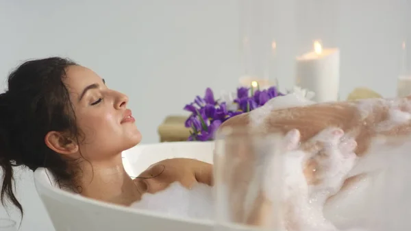 Closeup relaxed woman washing body with foam at home bath. Woman blowing foam