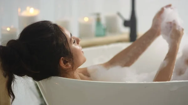Relaxed woman touching skin with foam. Brunette woman washing hands in bath — стокове фото