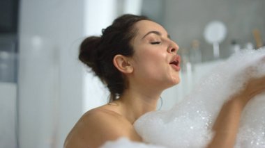 Yakından seksi bir kadın küvette köpük üflüyor. Baloncuklarla oynayan seksi kız
