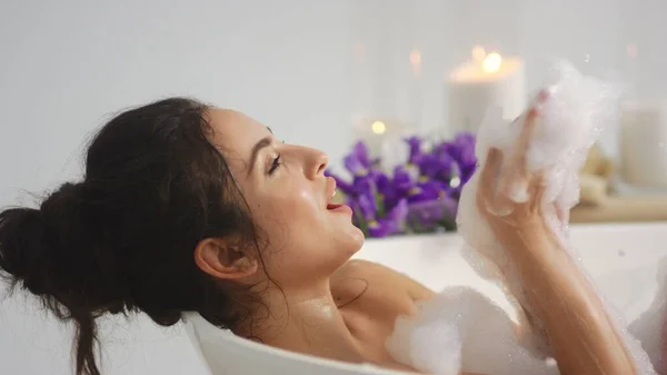 Vista lateral da mulher relaxada brincando com espuma. Mulher bonita sorrindo na banheira — Fotografia de Stock