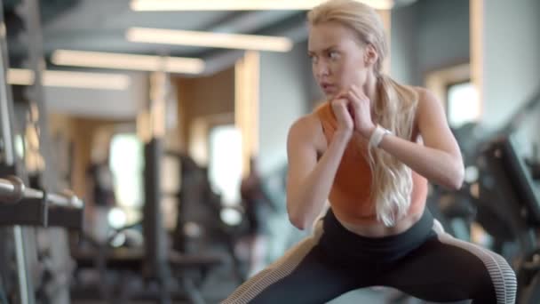 Ernsthafte Fitness-Frau macht Kniebeugen im Fitnessstudio. Sportliches Mädchen wärmt sich im Sportverein auf — Stockvideo