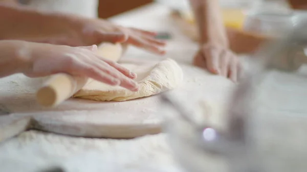 Mother teaching daughter to roll dough with rolling pin on kitchen table — Stockfoto