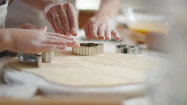 Close up woman and girl hands cutting dough with cookie cutters on kitchen table — Stockfoto