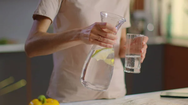 Vrouw die water in glas giet uit kruik. Vrouwe drinkwater thuis — Stockfoto