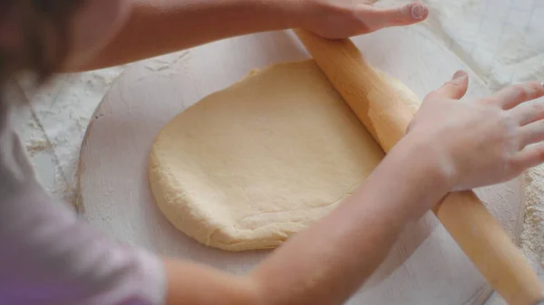 Дівчина рука обкатує тісто на столі з матір'ю на кухні. Сім'я готує вдома — стокове фото