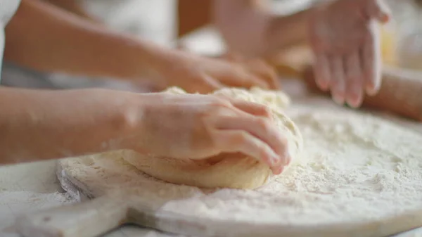 Woman helping daughter to knead dough with flour on kitchen table — Stockfoto