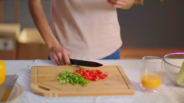 Dona de casa cortando legumes em tábua de madeira na cozinha. Senhora comendo tomate — Fotografia de Stock