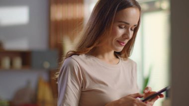 Mutfakta akıllı telefondan mesaj atan bir kadın. Evde cep telefonu kullanan bir bayan.