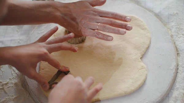 Closeup woman and girl cutting dough with cookie cutters on kitchen table — Stockfoto