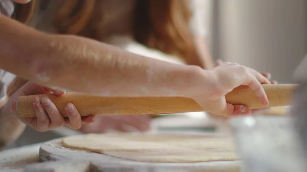 Woman teaching girl to roll dough on kitchen table. Girl hands using rolling pin — Stockfoto