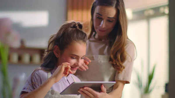Anne ve kızı mutfakta tablet kullanıyorlar. Evde kızla konuşan bir kadın. — Stok fotoğraf