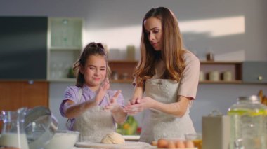 Smiling woman and girl shaking off flour on kitchen. Daughner helping mom.