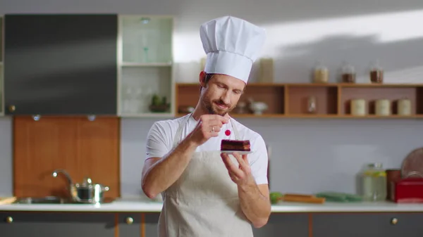 Baker putting cherry on cake at workplace. Chef man smiling at camera on kitchen — Φωτογραφία Αρχείου
