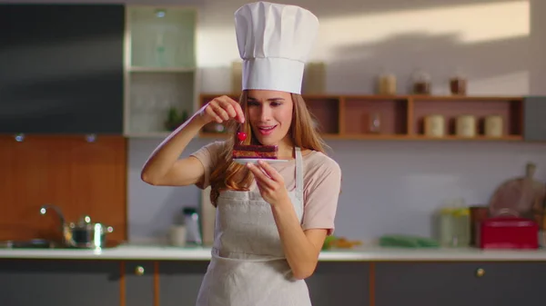 Baker decorating cake with cherry on kitchen. Chef woman in finishing dessert