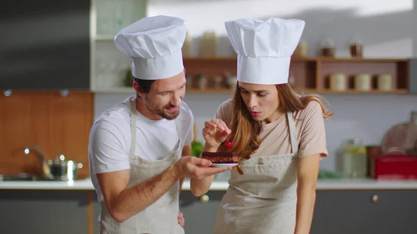 เบเกอร์และผู้ช่วยวางเชอร์รี่บนเค้กในครัว คู่ของขนมปัง — ภาพถ่ายสต็อก