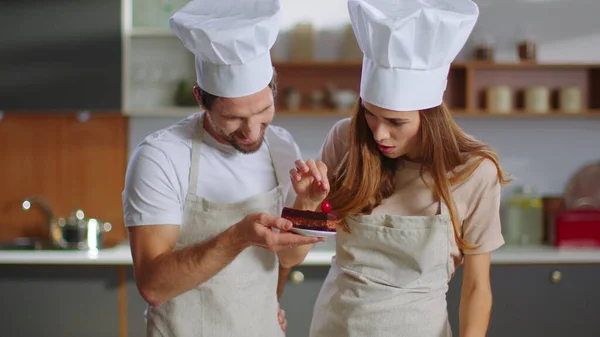 Portrait of confectioners decorating dessert with cherry on kitchen