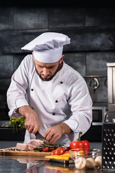 Chef cutting beef at kitchen. Chef in uniform cut steak at planked.