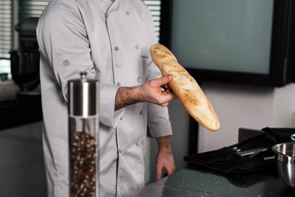 A séf keze a konyhában tartja a kenyeret. Szekrényszakács kéz francia kenyérrel. — Stock Fotó