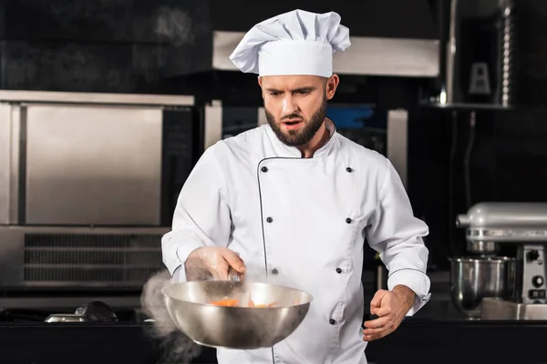 Szef kuchni przygotowuje jedzenie w kuchni restauracji. Poważny szef kuchni rzucający azjatyckie jedzenie. — Zdjęcie stockowe