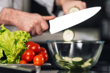 Aşçı elleri mutfakta yemek kesiyor. Yakından erkek elleri bıçakla salatalık doğruyor..