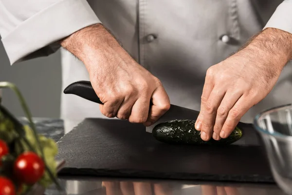 Chef cortando vegetais na cozinha. Fechar as mãos masculinas com faca fatia de pepino . — Fotografia de Stock