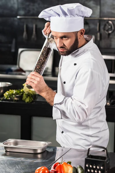 Chefe macho no restaurante da cozinha. Profissional com pepperbox pimenta comida . — Fotografia de Stock