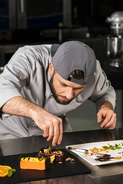 Chef man decorating cake at kitchen. Chef male making orange cake.