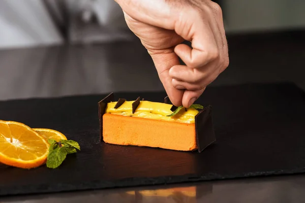Kokki kädet koristella oranssi kakku. Lähikuva kädet koristella jälkiruoka suklaalla. — kuvapankkivalokuva