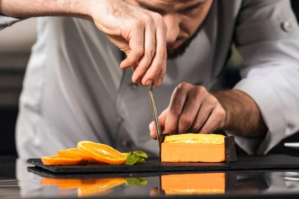 Chef macho decorar bolo na cozinha. Fechar as mãos chef fazer bolo de laranja . — Fotografia de Stock