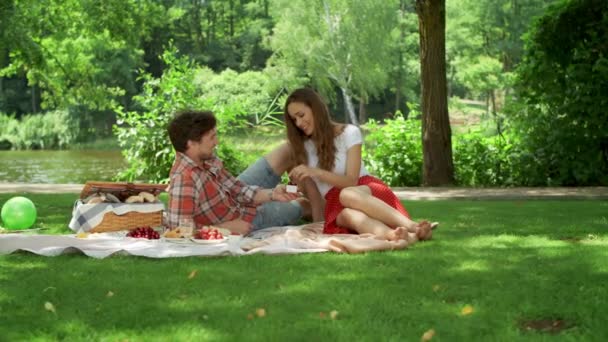 Το αγόρι και η φιλενάδα τρώνε κεράσια στο πικνίκ. ζευγάρι χαλαρωτικό σε εξωτερικούς χώρους — Αρχείο Βίντεο