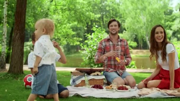 A család jól érzi magát a parkban. A testvérek szappanbuborékokkal játszanak az erdőben — Stock videók