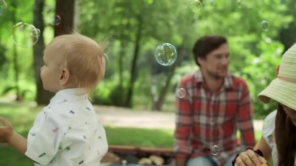 Batole si hraje venku s mýdlovými bublinami. Děti tráví čas s rodiči — Stock video