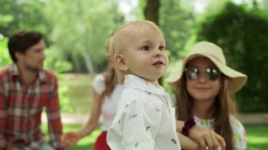 Kız ve bebek dışarıdaki kameraya bakıyor. Aile parkta birlikte dinleniyor.