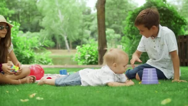 Tre bambini che giocano con i giocattoli nel parco. Bambino sdraiato sull'erba verde fuori — Video Stock