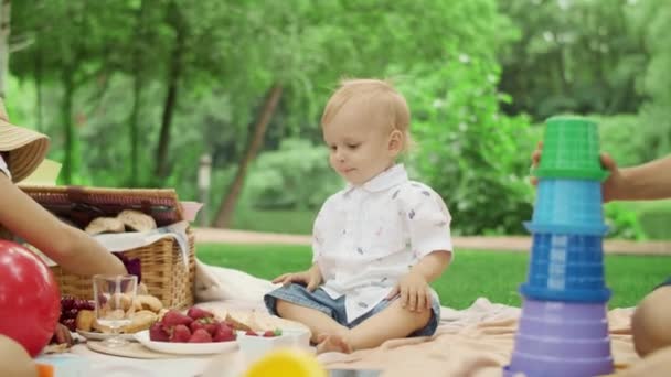 Bambini seduti su una coperta insieme nel parco. Bambino che prende la fragola dalla ciotola — Video Stock