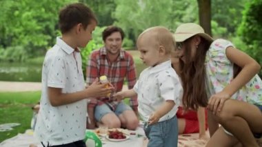 Mutlu kardeşler ormanda birlikte oynuyorlar. Gülümseyen aile dışarıda piknik yapıyor.