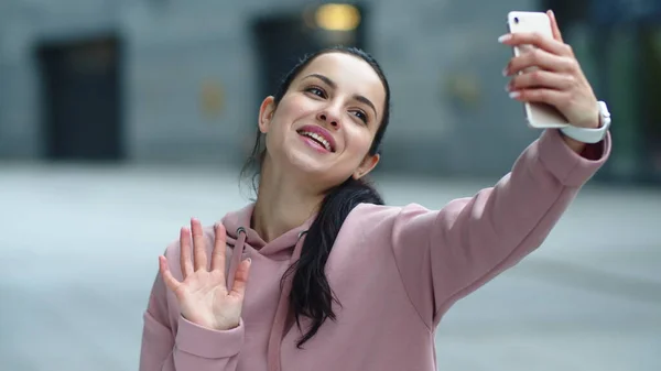 Una mujer sonriente saludando de la mano a la cámara. Chica feliz usando el teléfono móvil — Foto de Stock