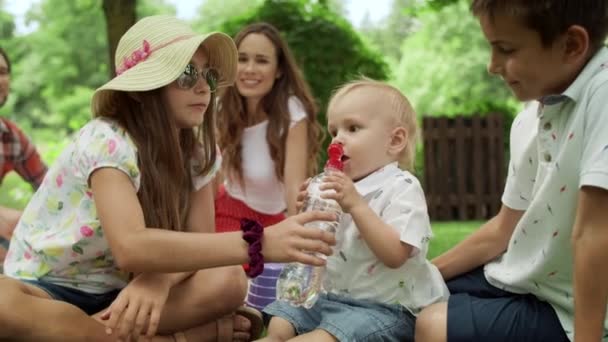 Familjen sitter på filt i parken. bedårande småbarn dricksvatten från flaska — Stockvideo