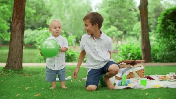 Два брата проводят время в летнем парке. Братья и сестры играют с мячом на открытом воздухе — стоковое видео