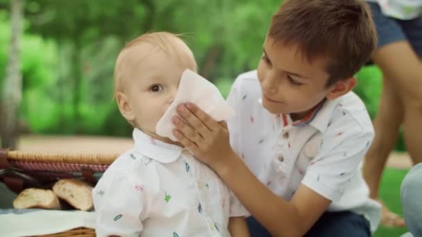 Bratr se stará o malého chlapce na pikniku. Matka ruka dávat třešeň na chlapce — Stock video